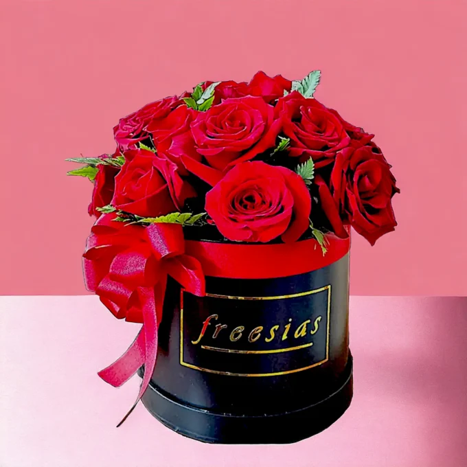 Arreglo floral de rosas rojas en elegante caja negro con una cinta roja, decorado para San Valentín.